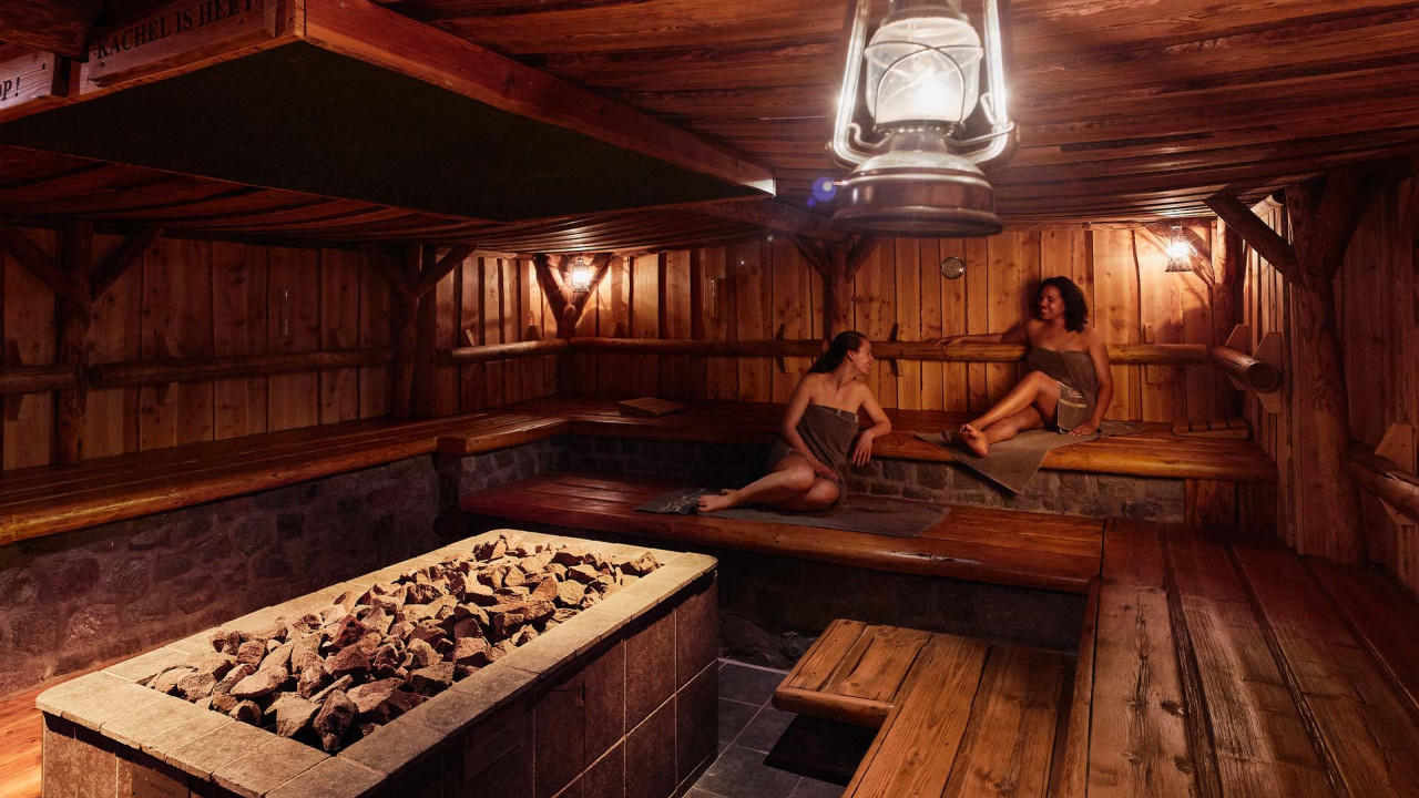 Mensen ontspannen in donkere sfeervolle sauna met stenen kachel