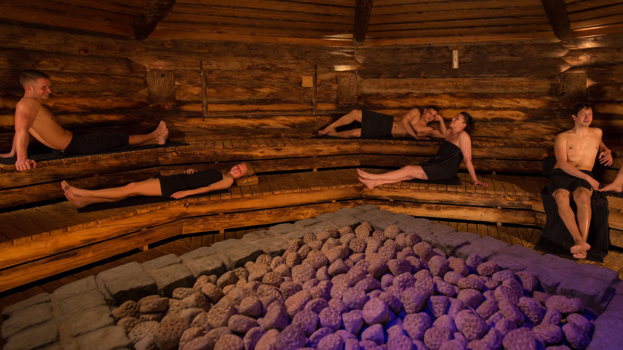 Mensen ontspannen in donkere sfeervolle sauna met stenen kachel