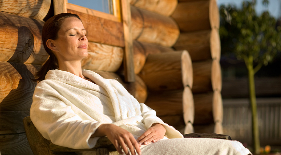 Vrouw geniet van het zonnetje in een stoel voor de sauna
